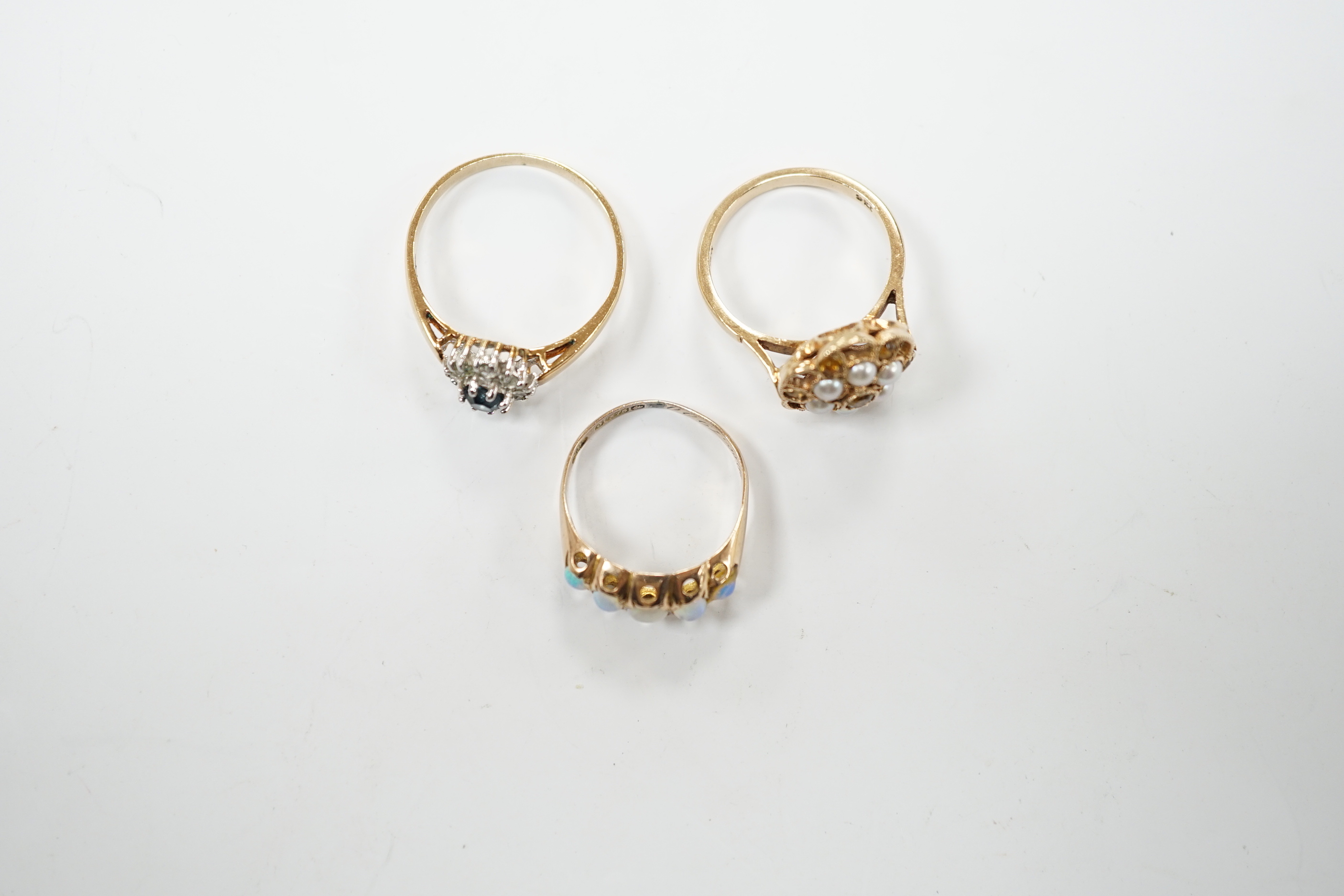A late Victorian 9ct gold and graduated five stone opal set half hoop ring, size L, a 9ct, seed pearl and citrine cluster set flower head ring, gross 4.7 grams and a costume ring.